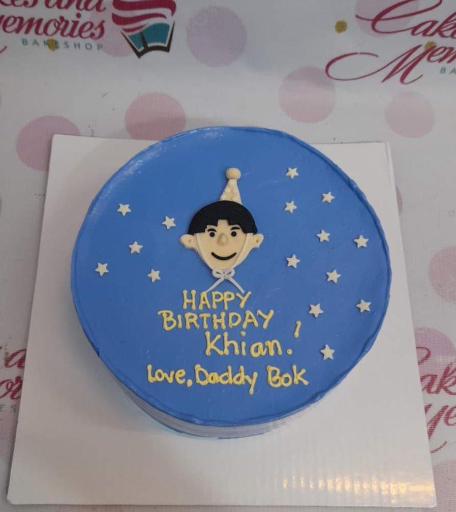 Blue bento cake with a 2D fondant boy character wearing a party hat, surrounded by white stars and yellow birthday message.
