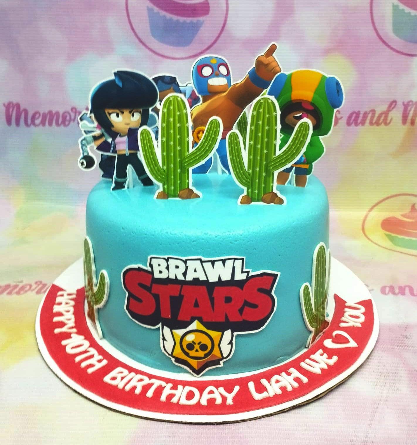 Light blue Brawl Stars themed birthday cake with character printouts, cactus toppers, and a red message banner on the base.