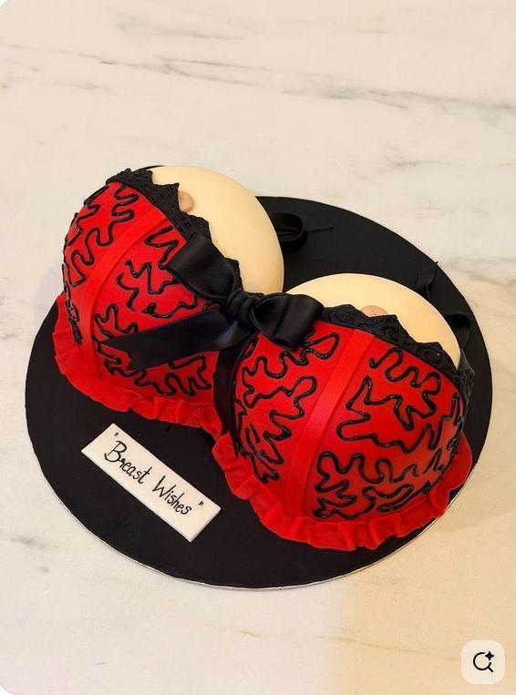 Novelty breast-shaped cake with red fondant lingerie, black lace icing, and a black bow.