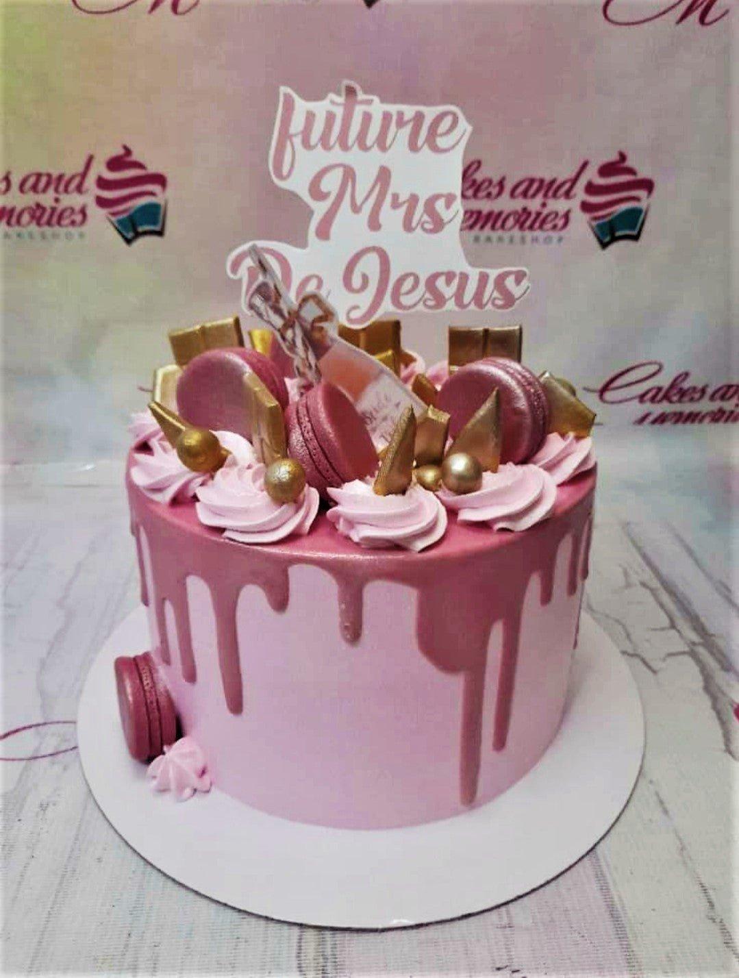 Pink drip cake for a future bride with pink macarons, gold chocolate bars, and a custom printout topper.
