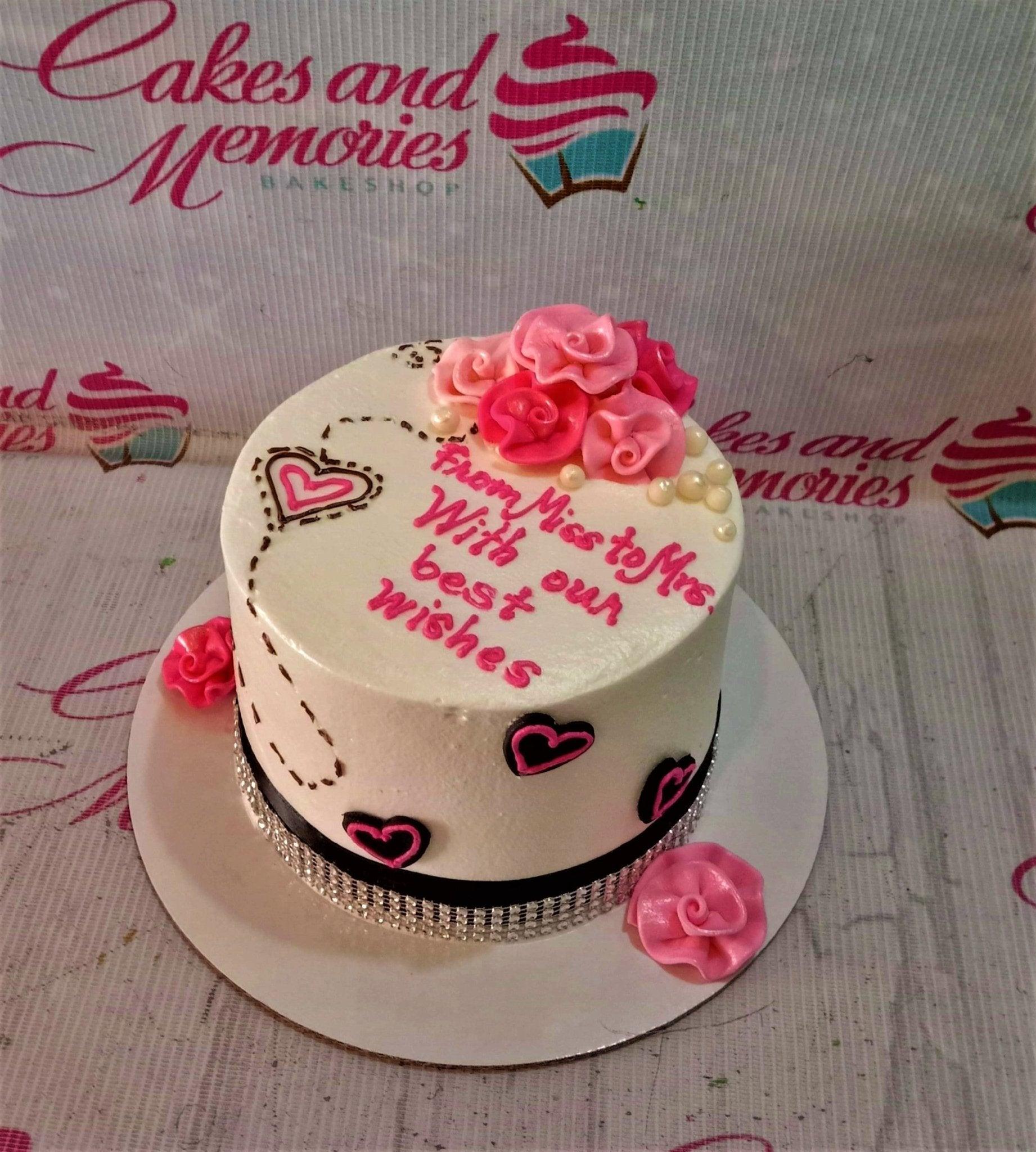 White soft-icing cake with pink fondant roses, black and pink hearts, and a bridal shower message.