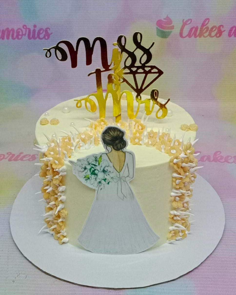 White minimalist bridal shower cake with a bride printout topper, gold Miss to Mrs topper, and yellow icing flower cascades.