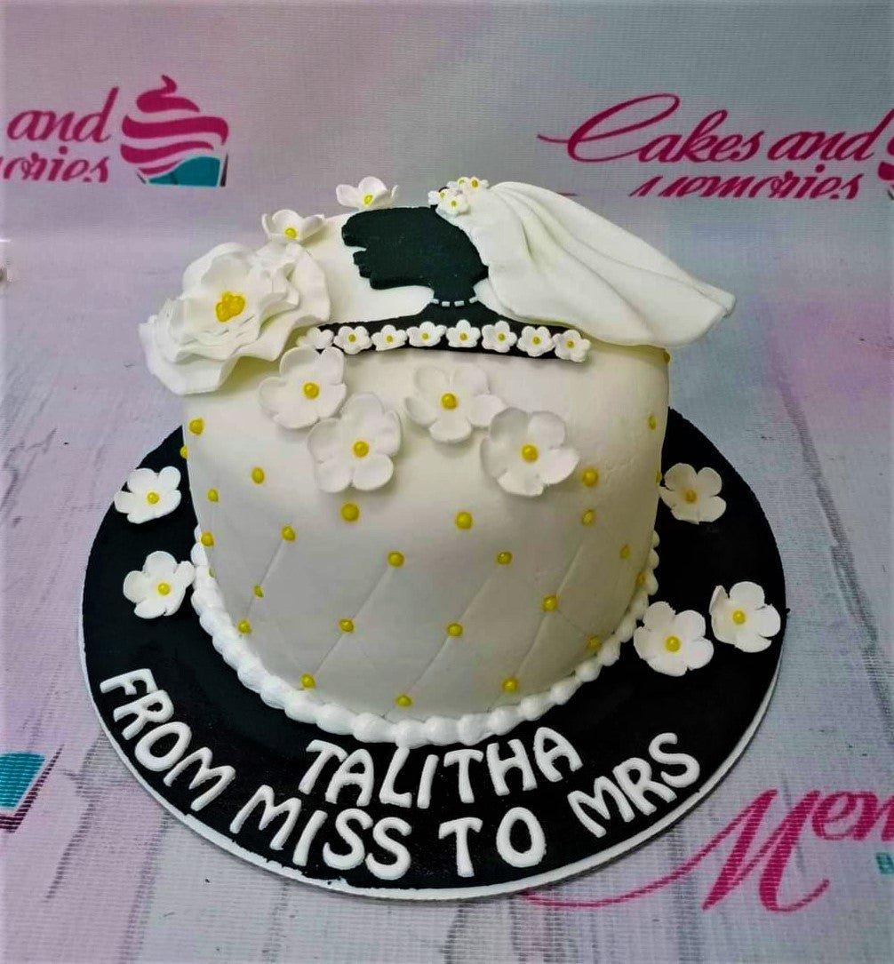 White fondant bridal shower cake with black silhouette bride topper, white gumpaste flowers, and yellow dots on a black base board.