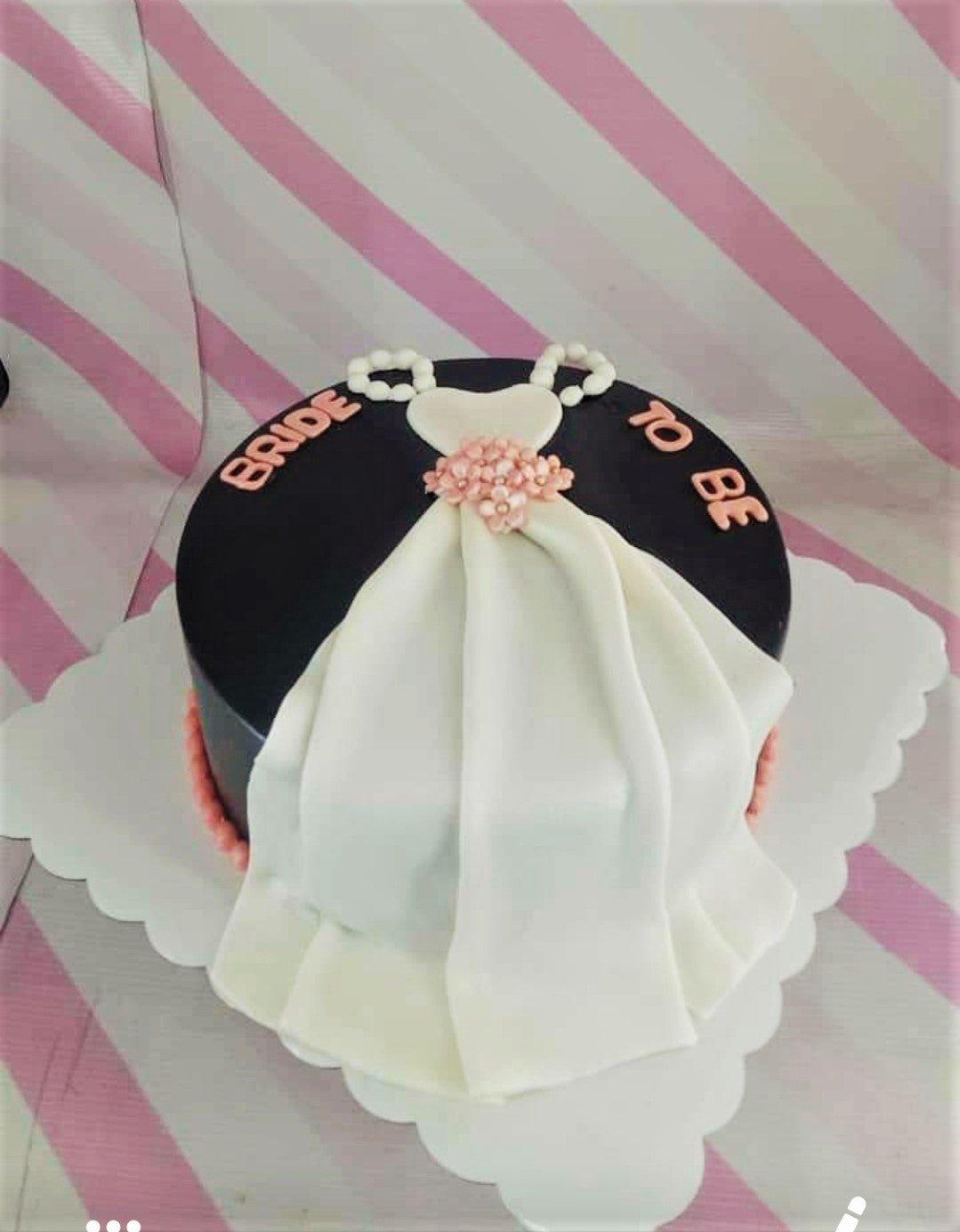 Black fondant cake with a white wedding dress design and pink floral accents for a bride-to-be celebration.