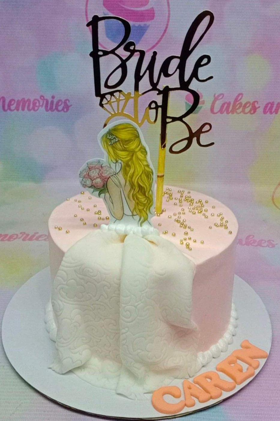 Pink bride-to-be cake with a blonde bride printout topper, white fondant dress drape, and gold dragees.