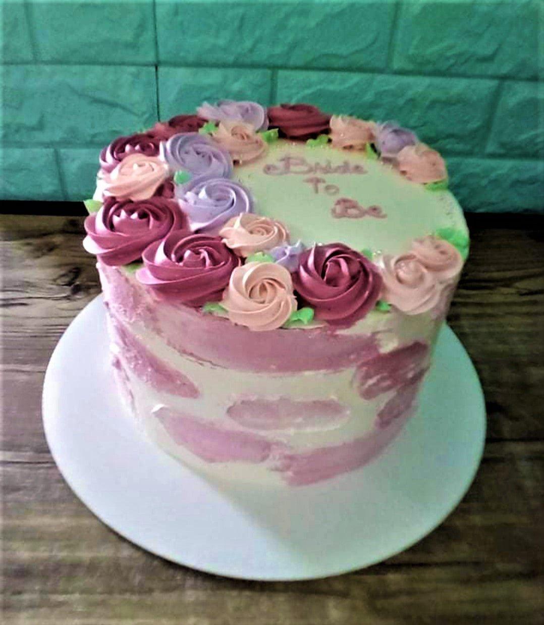 A single-tier white cake with pink watercolor icing strokes and a wreath of purple, pink, and hot pink icing rosettes on top.