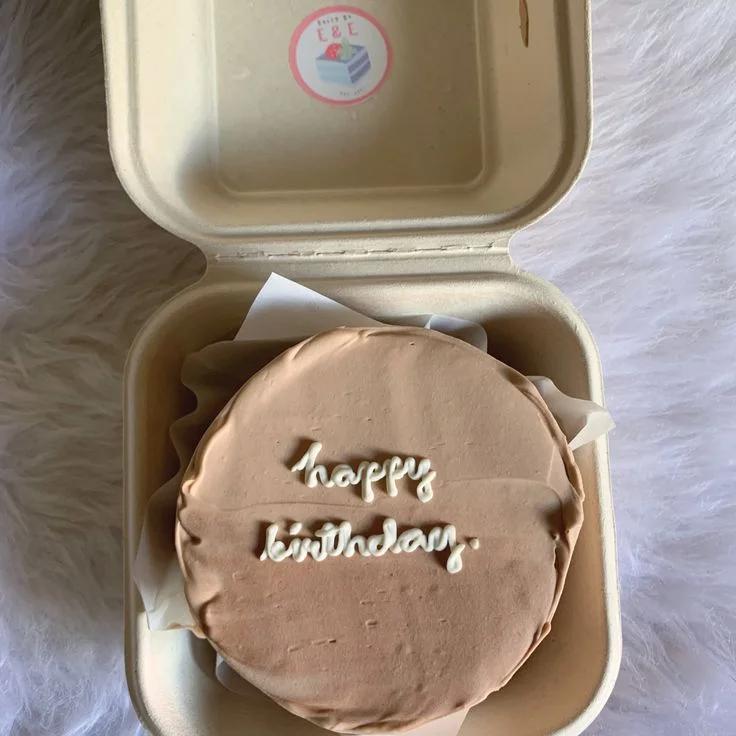 Minimalist brown bento cake with white piped icing text reading Happy Birthday in a compostable box.