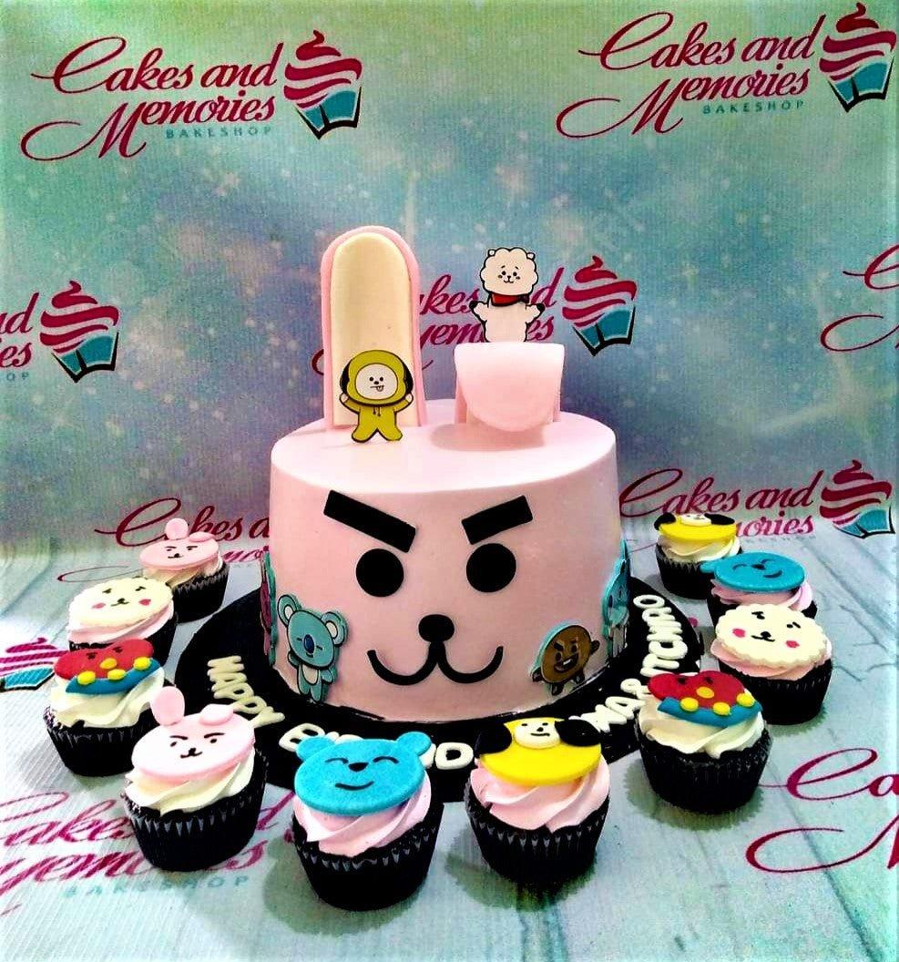 Pink BT21 themed cake with Cooky face design and character printouts, surrounded by matching character cupcakes.