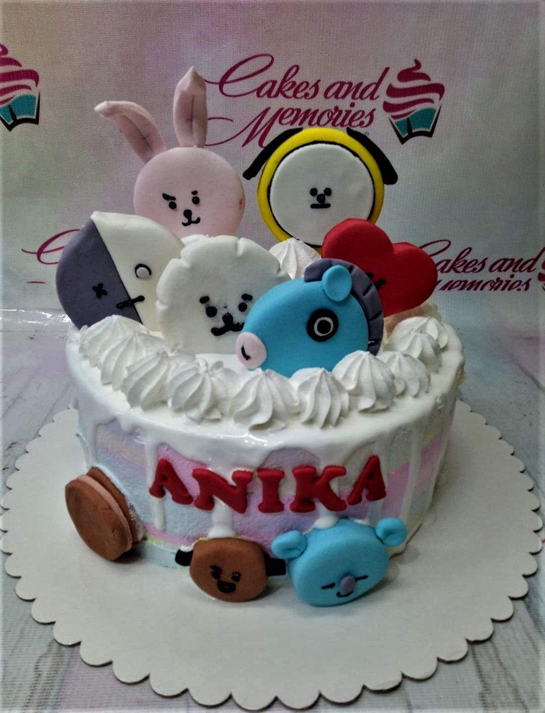 White soft-icing cake with BT21 character fondant toppers, white icing rosettes, and red gumpaste letters spelling ANIKA.