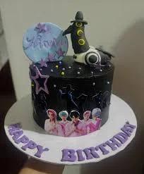 Black K-pop themed birthday cake with a 3D bird figure, purple stars, and a printed photo of a boy band on the side.
