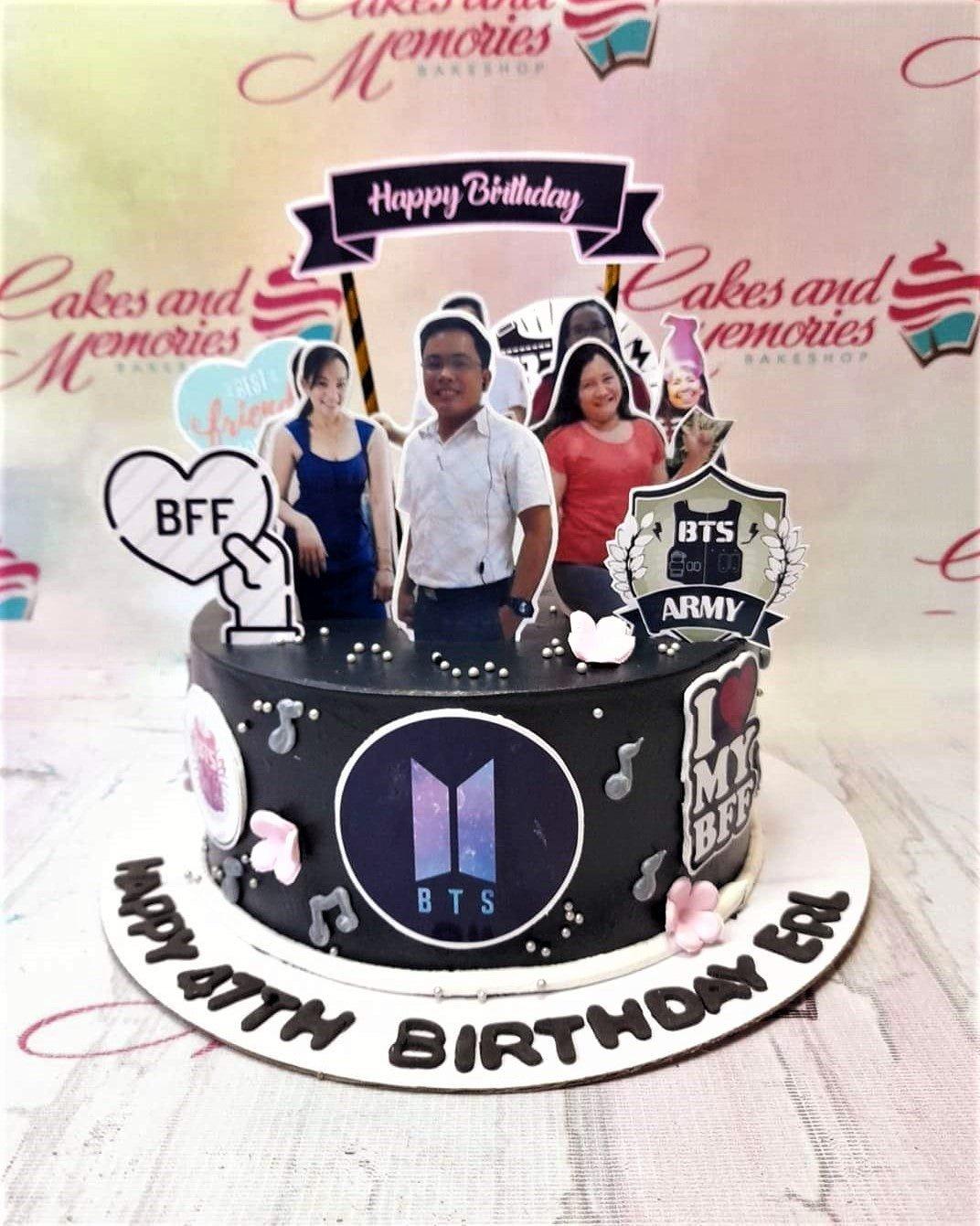 Black BTS Army themed birthday cake with photo printouts of friends, music notes, and a large BTS logo on the side.