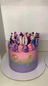 A single-tier birthday cake with a pink and purple gradient icing, topped with K-pop group printouts, a glittery number 10, and icing rosettes.
