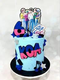 Light blue K-pop themed birthday cake for Koa featuring a group photo printout, musical notes, and stars in blue, pink, and black.