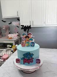 Light blue BTS K-pop themed birthday cake with character printouts and stylized logo on the side.