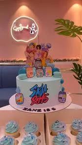 Light blue BTS K-pop themed birthday cake with character printouts, macarons, and a custom Saja Boys logo.