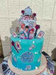 Teal K-pop themed cake with printed character toppers, lightsticks, and music notes for a fan celebration.