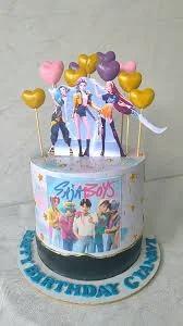 K-pop themed birthday cake with printed character toppers, gold hearts, and a photo print on the side.