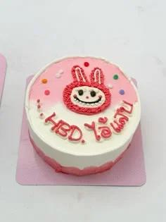 Pink and white bento cake with a hand-piped red bunny character and HBD message in Thai script.