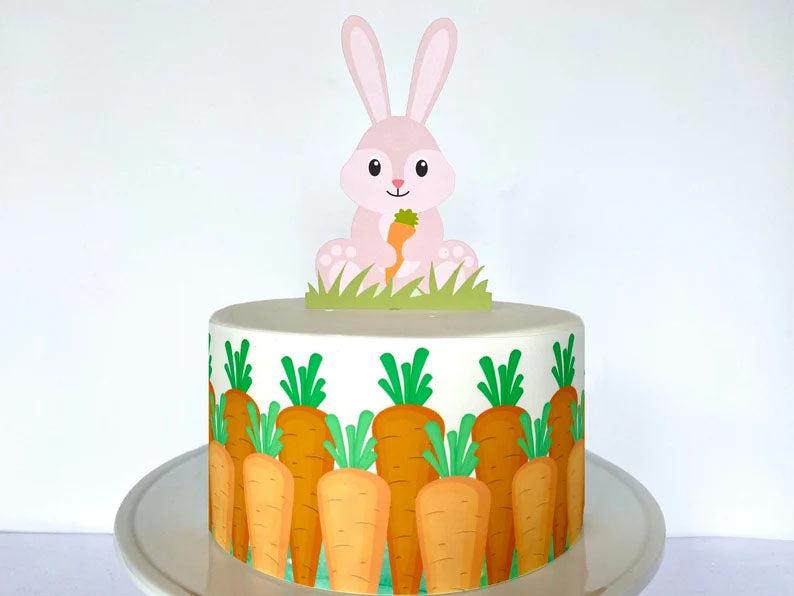 White single tier cake with a pink bunny printout topper and orange carrot gumpaste panels around the sides.