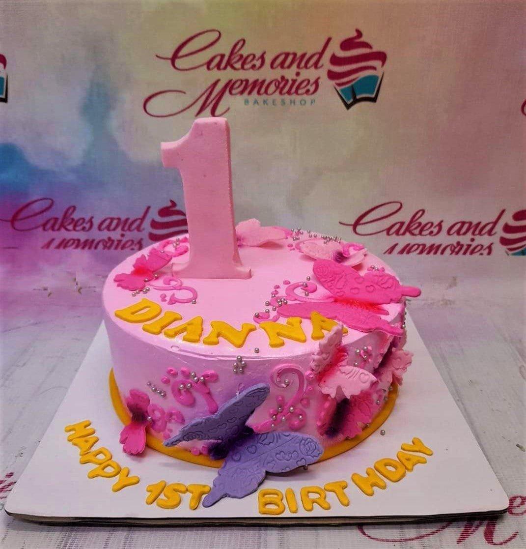 Pink butterfly birthday cake with a large pink number one topper and yellow icing message on a white board.