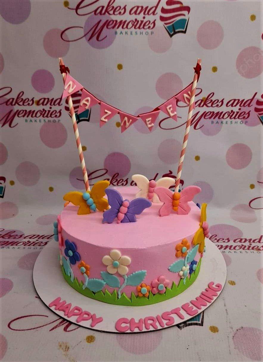 Pink 1-tier christening cake with fondant butterflies, flowers, and a pink banner topper.