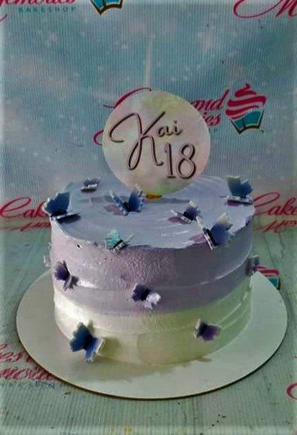 A single-tier purple and white ombre cake decorated with blue and purple butterflies and a large circular topper for an 18th birthday.