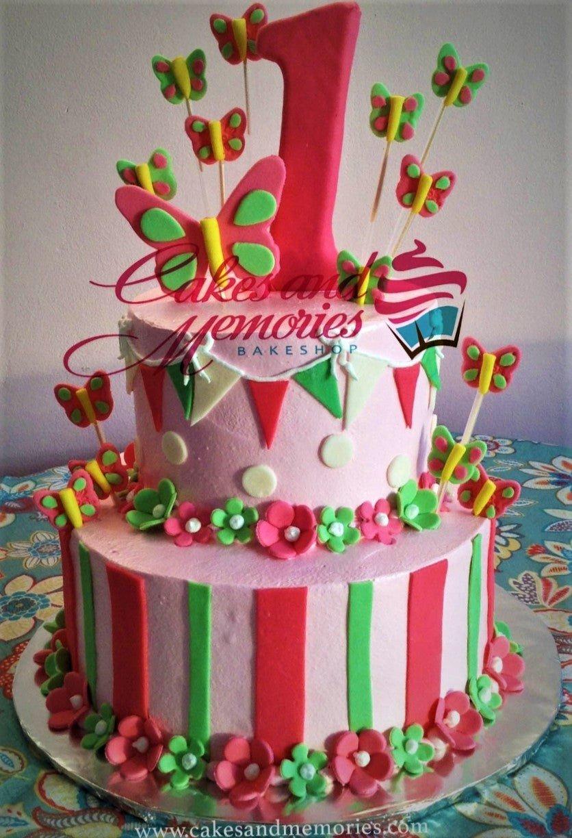 Pink two-tier birthday cake with colorful fondant butterflies, flowers, and a large number one topper.