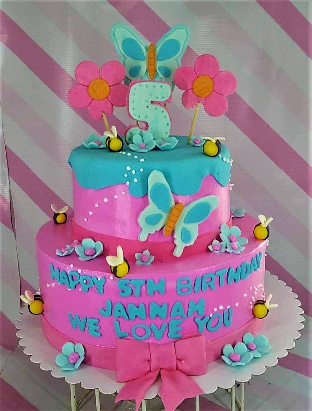 Two-tier pink and blue garden themed cake with fondant flowers, butterflies, and bees for a 5th birthday.