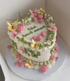 Heart-shaped white soft-icing cake with pink and yellow butterflies, pink mushrooms, and green piped vines.