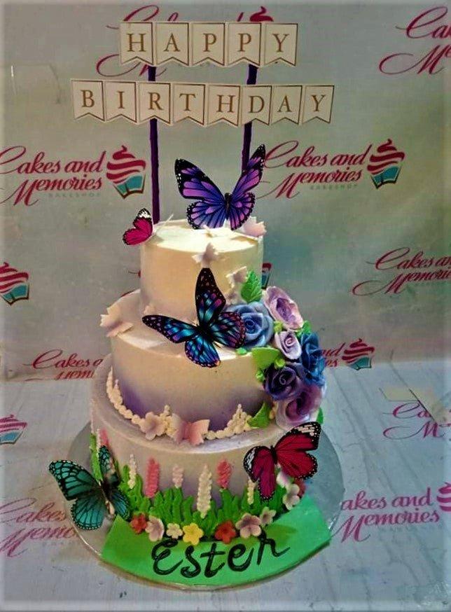 3-tier purple and white butterfly garden cake with edible flowers and a Happy Birthday banner topper.