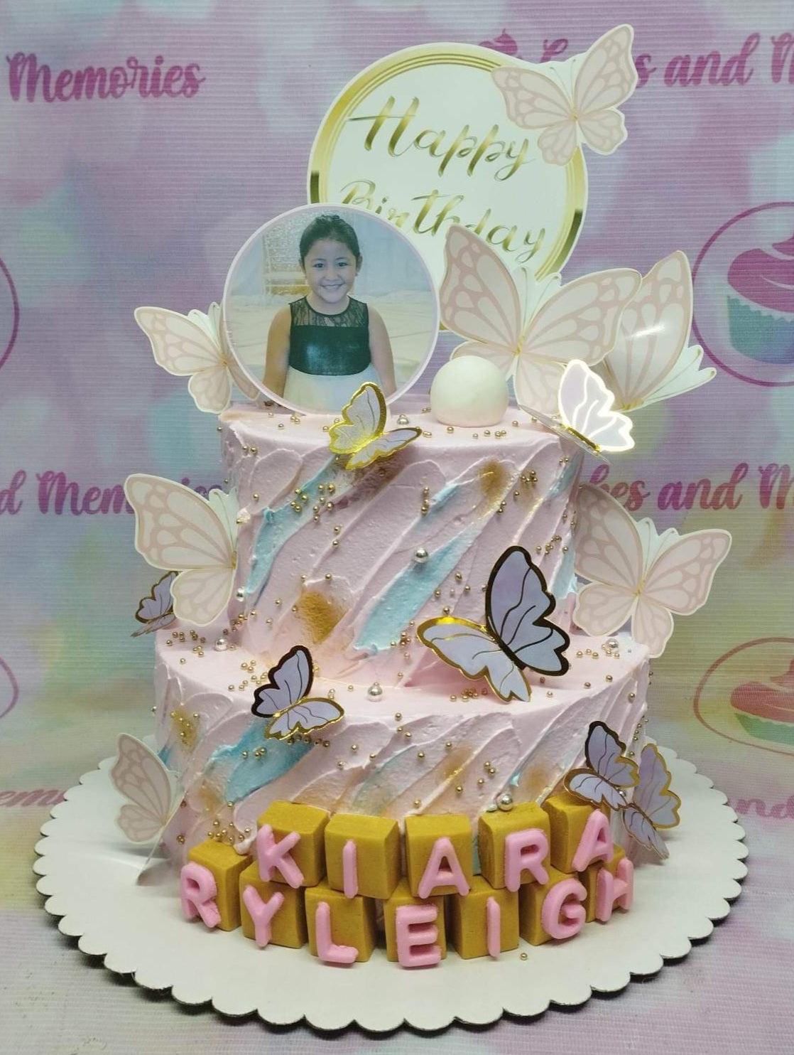Pink 2-tier butterfly birthday cake with a photo printout topper, gold dragees, and pink gumpaste name blocks.