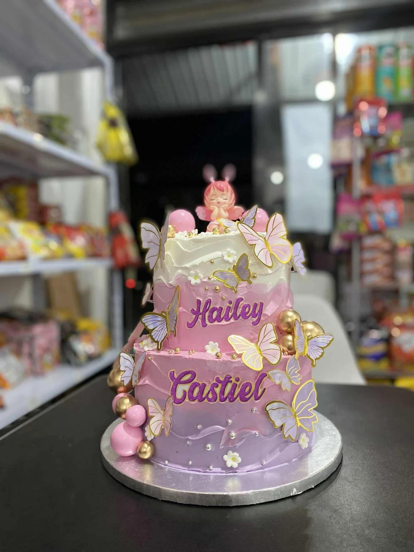 Two-tier pink and purple gradient cake decorated with paper butterflies and a sleeping baby topper