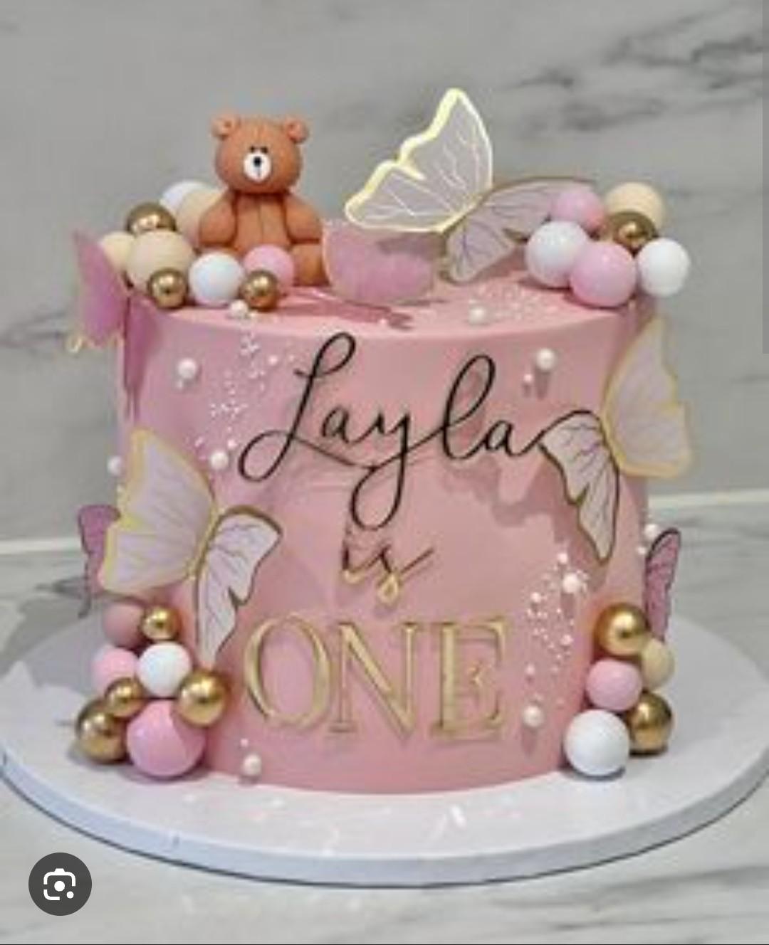 Pink 1st birthday cake for Layla featuring a fondant teddy bear, butterflies, and pink, white, and gold decorative balls.