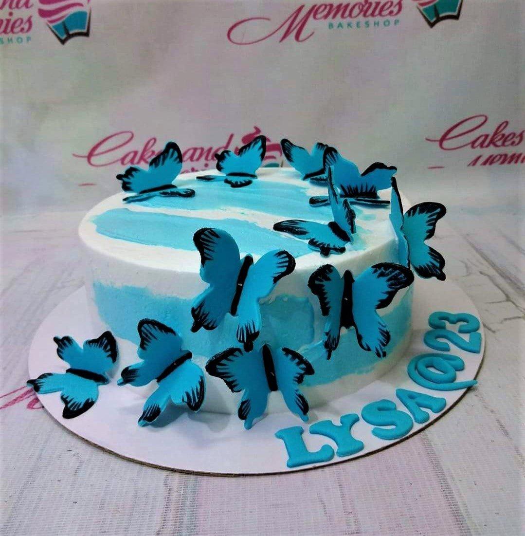 White and light blue butterfly cake with blue butterfly toppers and a personalized name on the base board.
