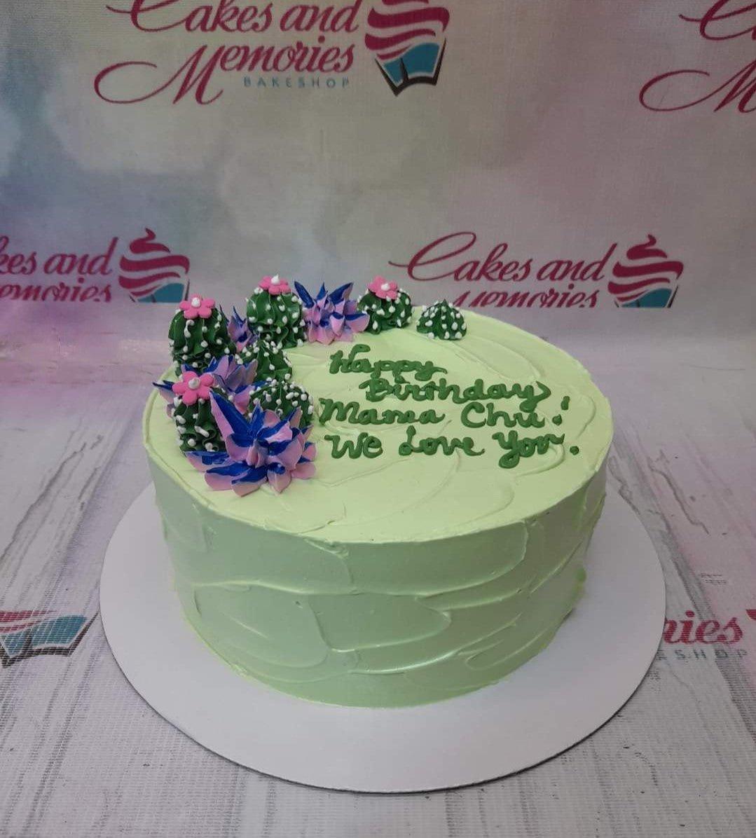 Light green 1-tier birthday cake with piped icing cactus and succulent decorations and a green birthday message.