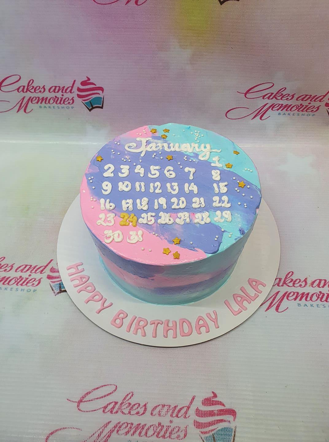 Bento calendar cake with pink, blue, and purple watercolor icing, white piped January calendar, and gold star accents.