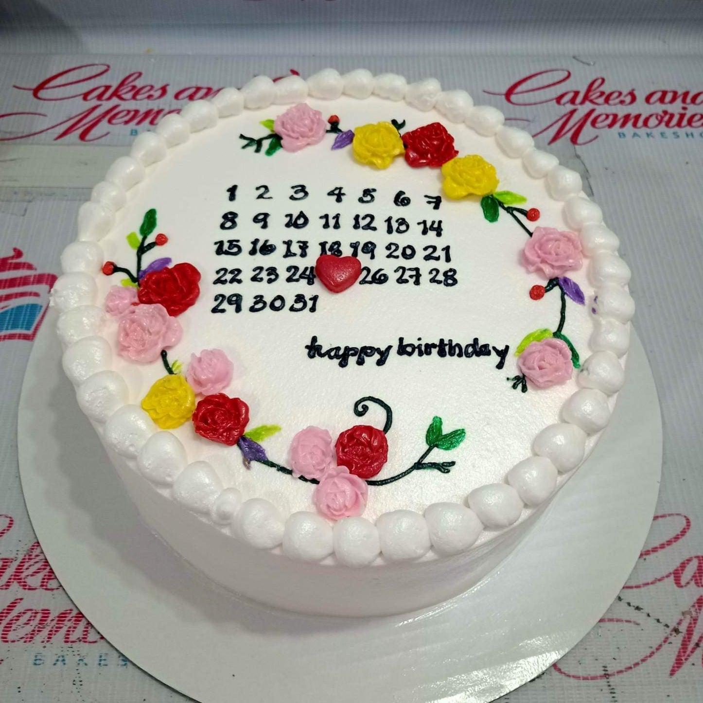 White round minimalist calendar cake with piped icing flowers in red, pink, and yellow with a black calendar design and a red heart.