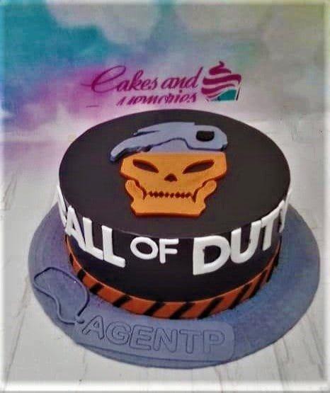 Black Call of Duty themed cake with orange skull logo and white lettering on a gray base board.