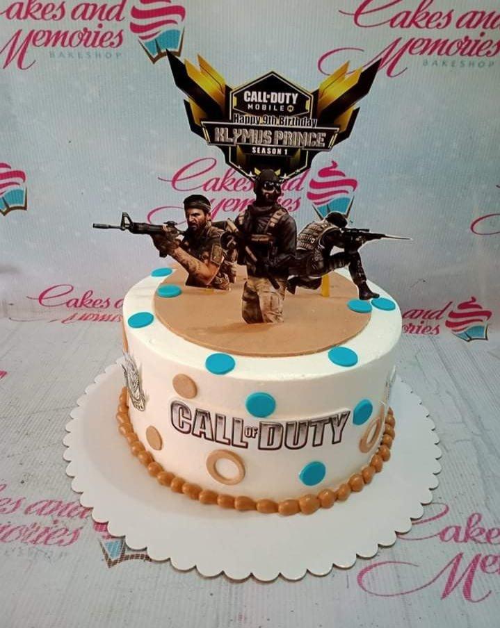Call of Duty Mobile themed birthday cake with soldier printouts, logo, and blue and tan fondant dots on white icing.