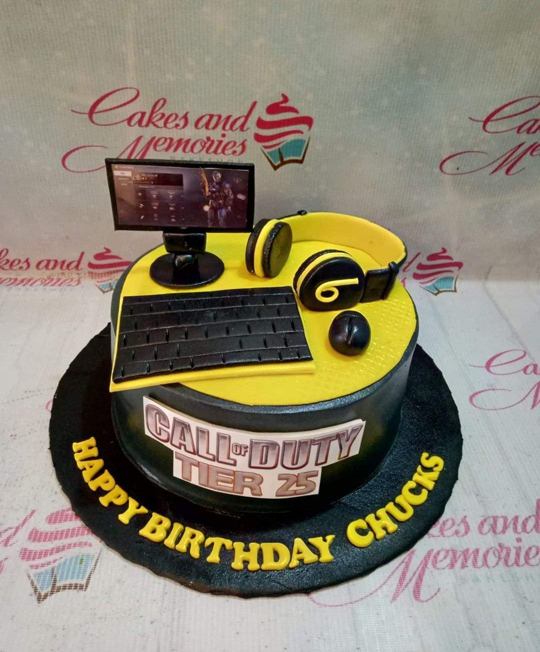 Black and yellow Call of Duty themed birthday cake with fondant gaming accessories like a monitor, keyboard, and headset.