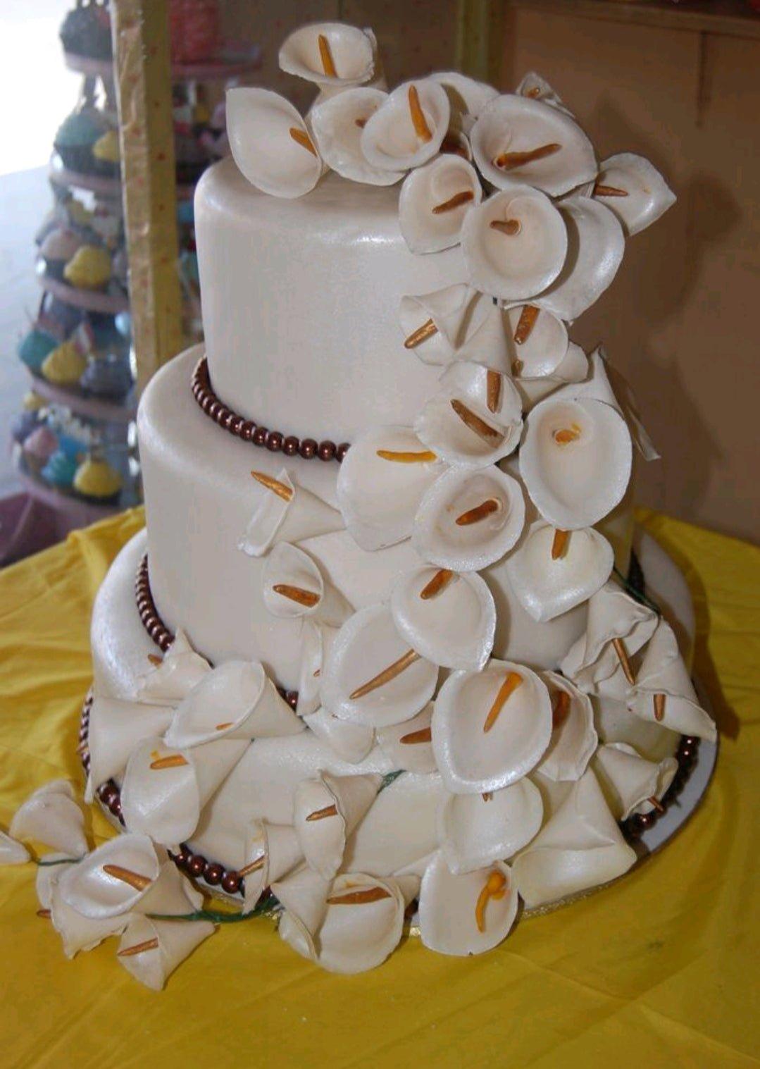 Elegant three-tier ivory fondant wedding cake adorned with a cascading waterfall of white gumpaste calla lilies and brown pearl borders.
