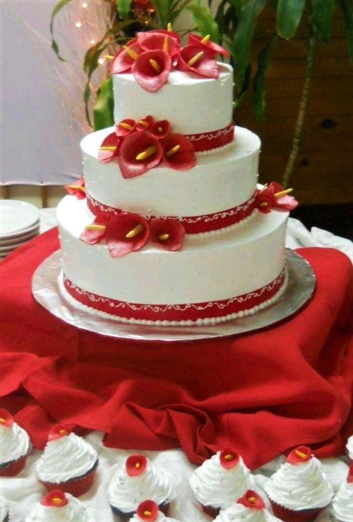 Elegant 3-tier white wedding cake decorated with vibrant red gumpaste calla lilies and red ribbon borders.