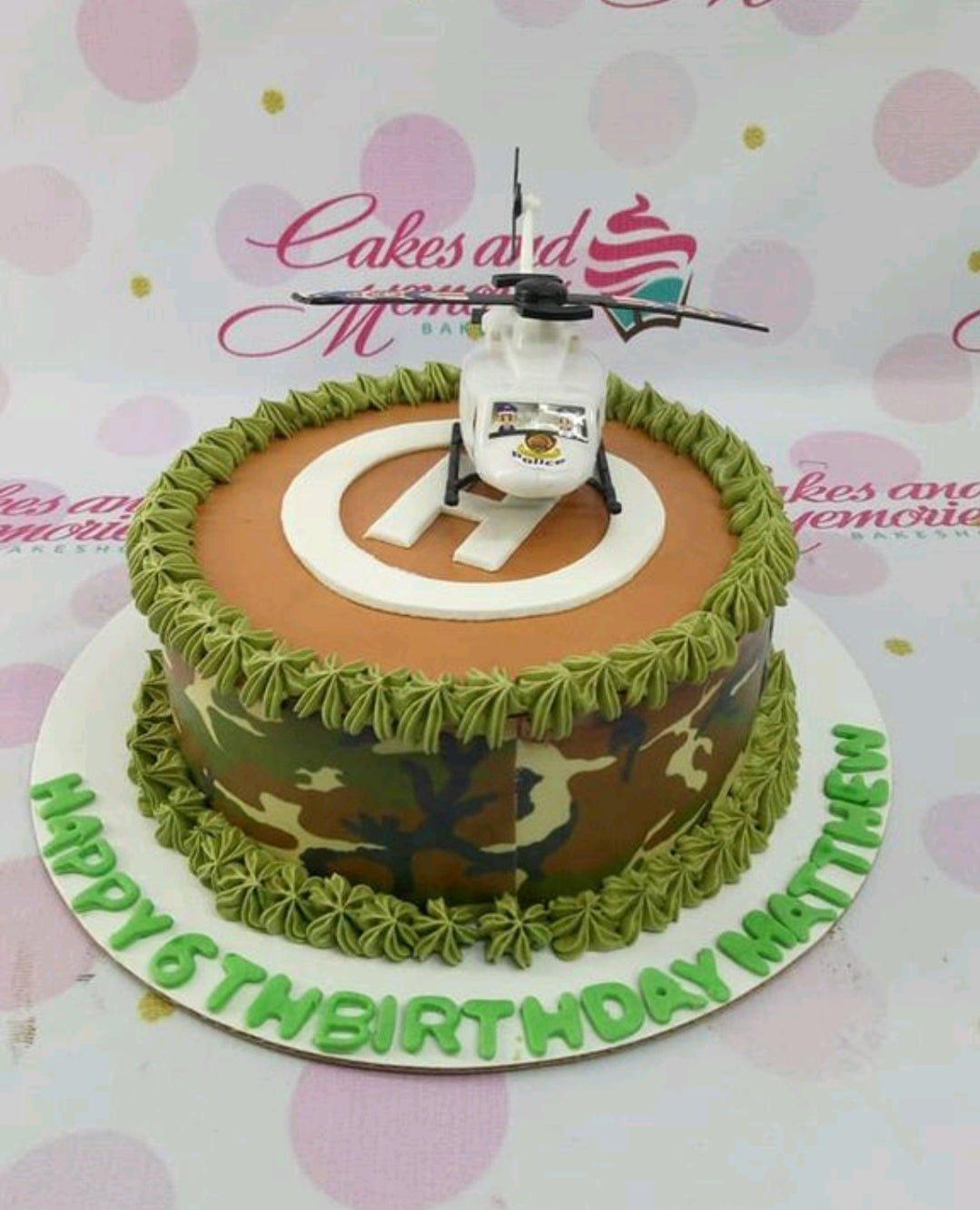 Camouflage military themed cake with a white police helicopter toy topper and green icing rosettes.