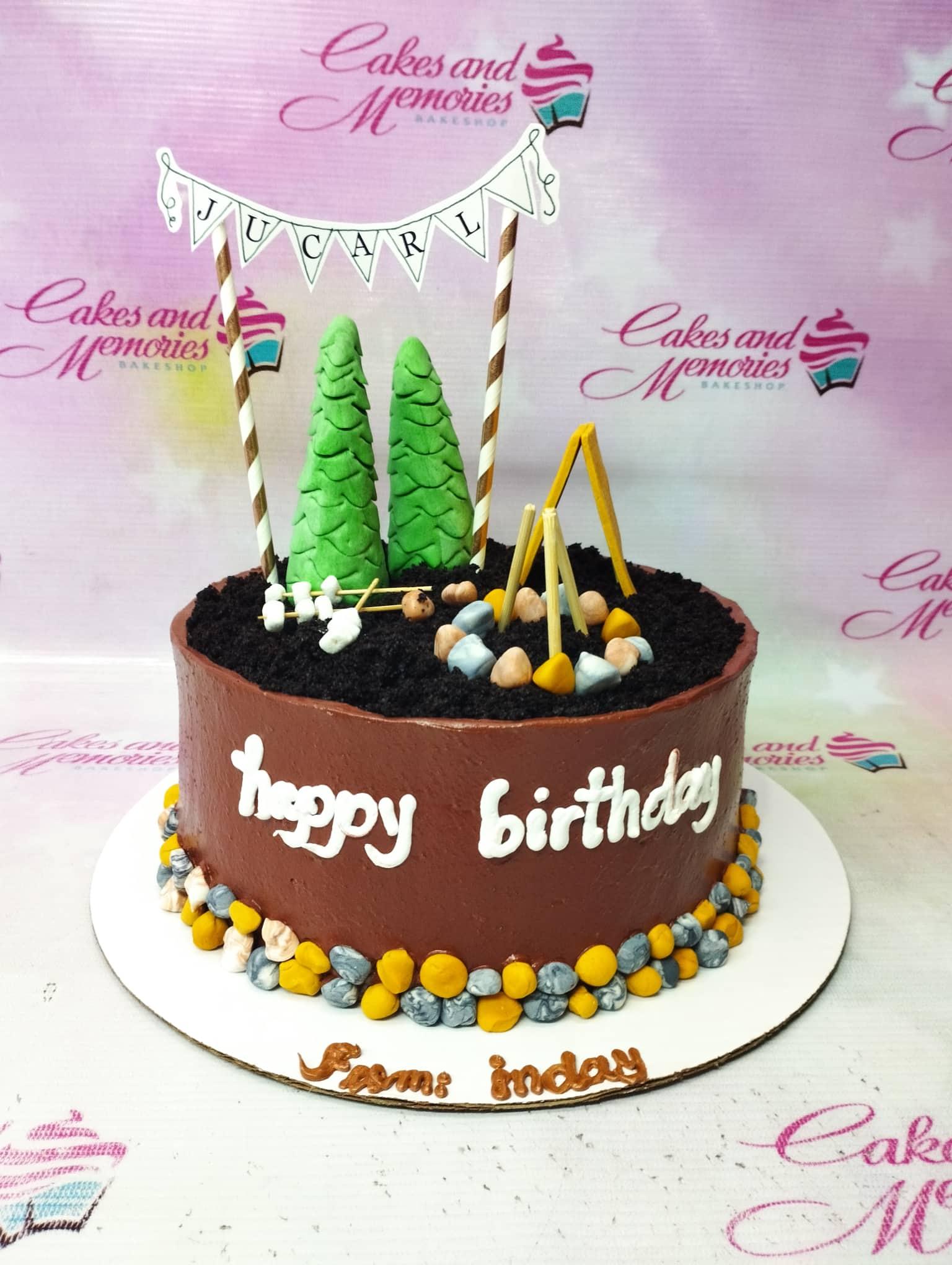 Brown camping themed birthday cake with fondant pine trees, a campfire, and a personalized name banner.