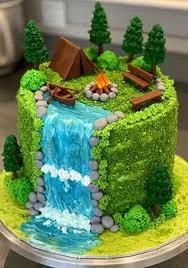 A creative camping-themed cake featuring a textured green icing forest, a blue icing waterfall, a brown fondant tent, and miniature evergreen trees.