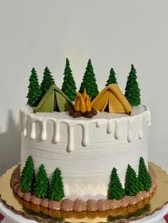 White 1-tier camping themed cake with green fondant pine trees, a yellow and green tent, and a small campfire topper.