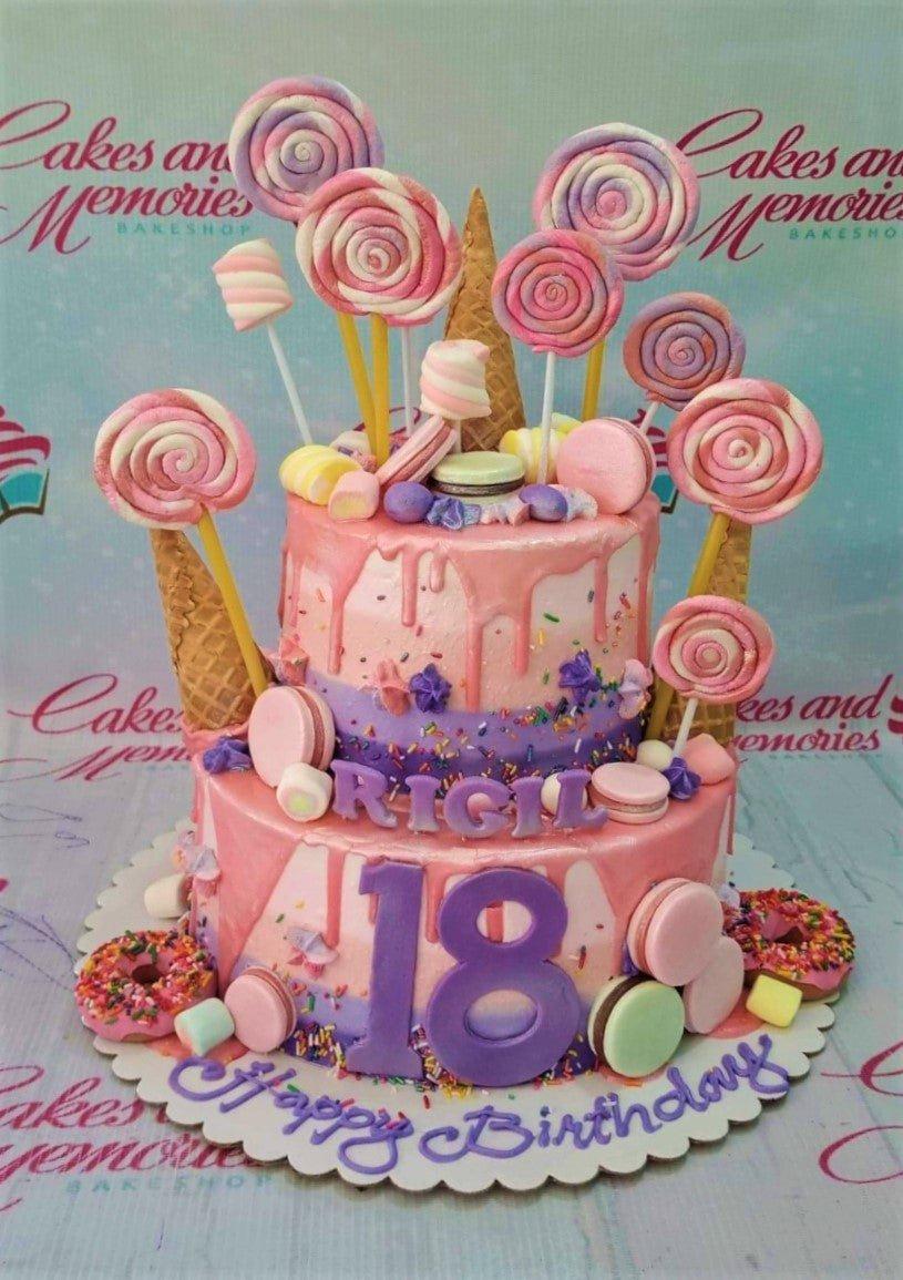 Two-tier pink and purple candy-themed cake with lollipops, macarons, donuts, and a large purple number 18.