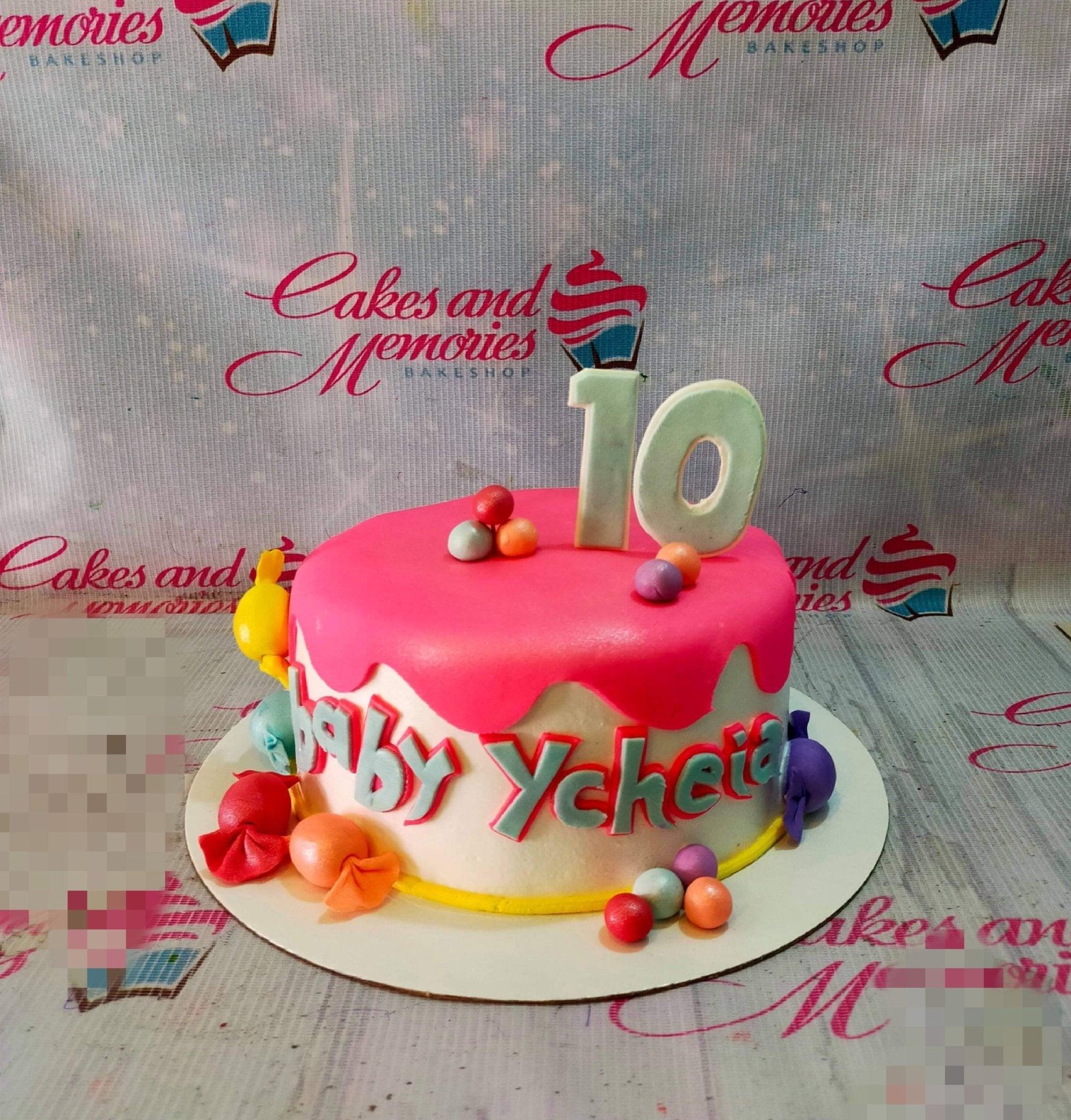 Pink and white birthday cake with fondant candy decorations and a large number 10 topper.