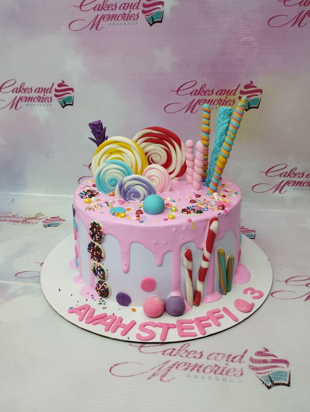 Pink and white candy-themed cake with colorful fondant lollipops, candy canes, and sprinkles.