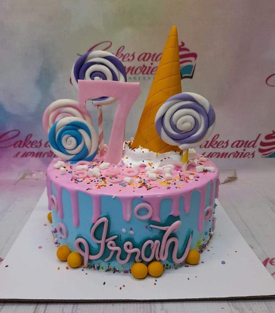 Light blue birthday cake with pink drip, colorful lollipops, a yellow cone, and a pink number 7 topper.